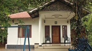 A white building with a red-tiled roof, two wooden doors, and a porch with two chairs. - Wayanad days Holiday Home with Tree Hut and Tent

 (Mananthavady)