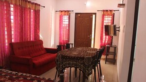 A room with a red sofa, a round table with chairs, and a door. - Wayanad days Holiday Home with Tree Hut and Tent

 (Mananthavady)