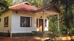 A single-story building with a tiled roof, a porch with a wooden roof, and a door with a window. - Wayanad days Holiday Home with Tree Hut and Tent

 (Mananthavady)
