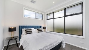 Un dormitorio con una cama grande, dos mesitas de noche y un ventanal con vidrio esmerilado.