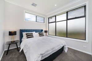 Un dormitorio con una cama grande, dos mesitas de noche y un ventanal con vidrio esmerilado.