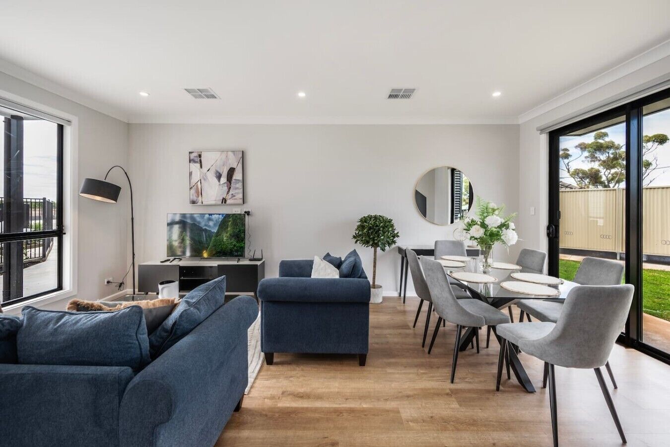 Een moderne woonkamer met een bank, een televisie en een eethoek met stoelen en een tafel.