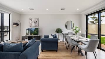 Een moderne woonkamer met een bank, een televisie en een eethoek met stoelen en een tafel.