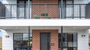 Un edificio de dos pisos con fachada de ladrillo, ventanas amplias y un balcón con barandillas de metal.
