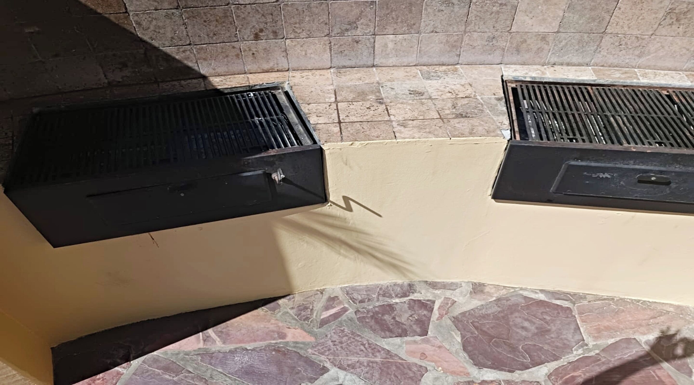 A stone-tiled wall with two black grill vents.