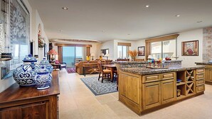 A spacious kitchen with wooden cabinets, a granite countertop, and a large island. There is a dining area with a table and chairs, and a view of the ocean through large windows. - Condo Bella Sirena 805 C by Kivoya (Puerto Peñasco)