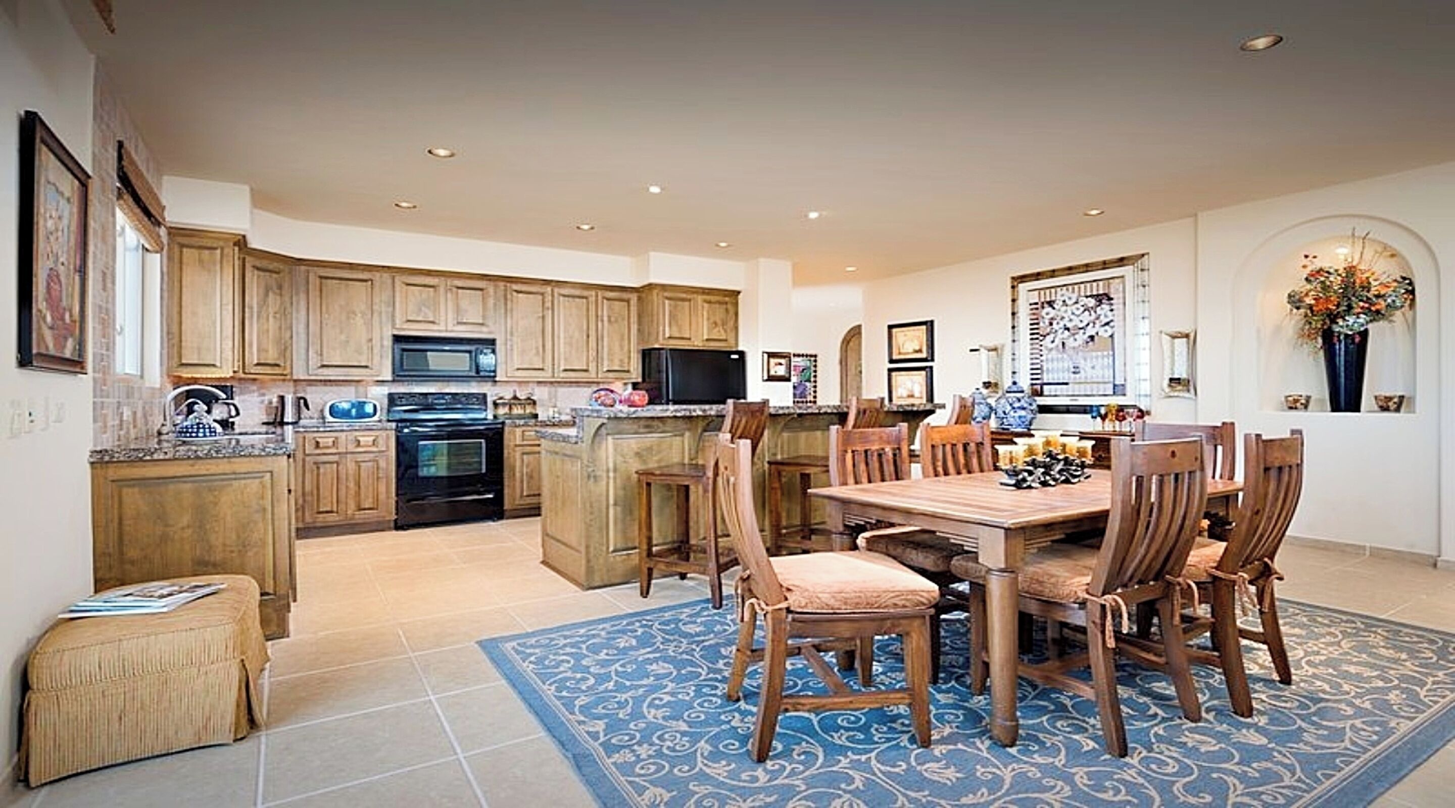 A spacious kitchen with wooden cabinets, a central island, and a dining area with a blue patterned rug.