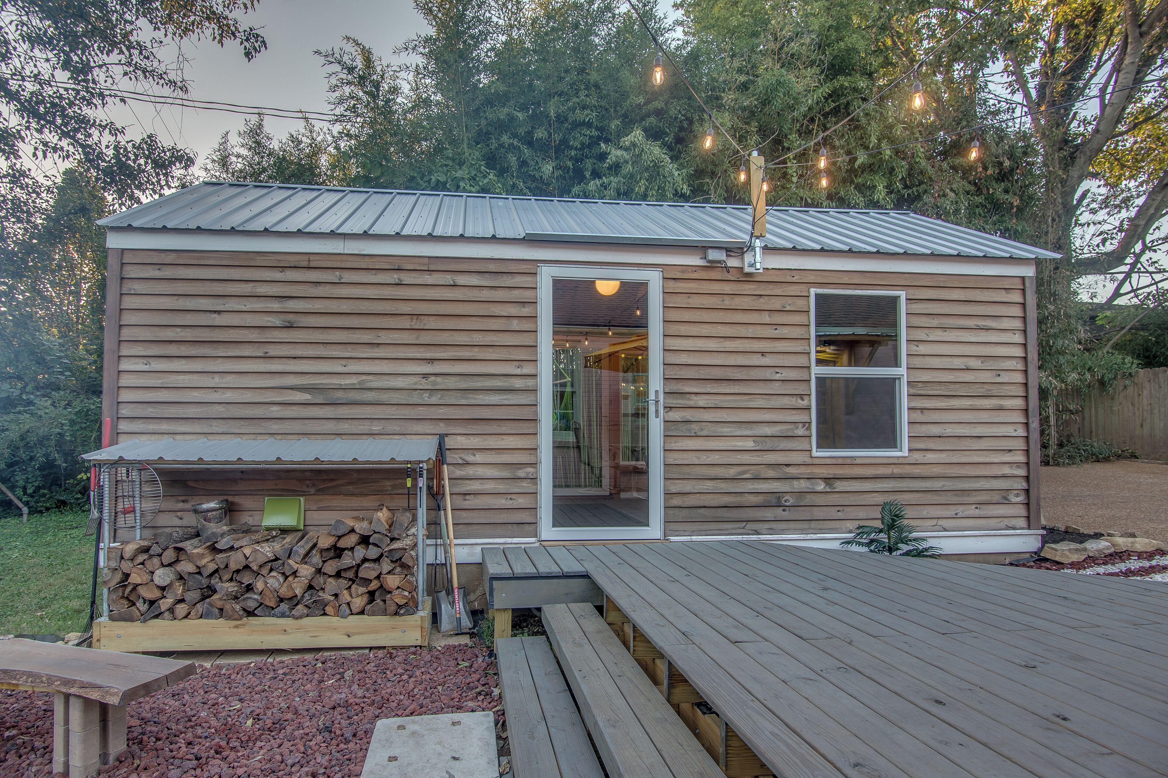 A wooden cabin with a metal roof, a door, and a window. There is a deck in front of the cabin.
