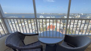 Een balkon met rieten stoelen en een kleine tafel, met uitzicht op een jachthaven met boten en gebouwen.