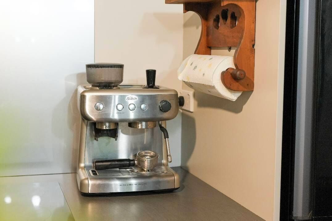 Een roestvrijstalen espressomachine met een koffiekan erop, een bedieningspaneel met knoppen en draaiknoppen, en een klein waterreservoir.