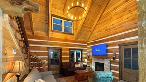 A log cabin interior with a staircase, a fireplace, a television, and a cozy seating area.