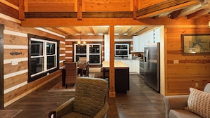 A log cabin interior with a dining area, kitchen, and a large window.