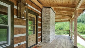 A wooden cabin with a stone pillar, a wooden deck, and a glass door.