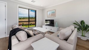 Un salon comprenant un canapé, une table basse, un tél éviseur et une grande fenêtre donnant sur une clôture et de la verdure.