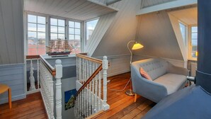 A high-ceilinged room with a wooden staircase, a model ship, and a lamp.
