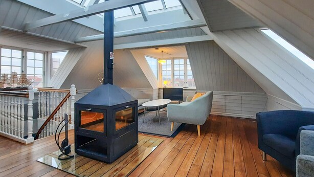 A loft-style room with a black wood-burning stove, a round dining table, and a blue armchair.