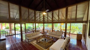 A spacious indoor area with a high ceiling, wooden beams, and large windows. There are multiple seating areas with sofas and tables, and a central coffee table. - Spacious Gated Casa de Campo 5-bedroom Villa w/ Pool/Hot Tub and Hi speed WiFi (La Romana)