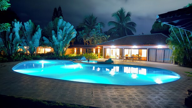 A swimming pool with a tiled deck, surrounded by tropical plants and a building with a tiled roof and large windows. - Spacious Gated Casa de Campo 5-bedroom Villa w/ Pool/Hot Tub and Hi speed WiFi (La Romana)