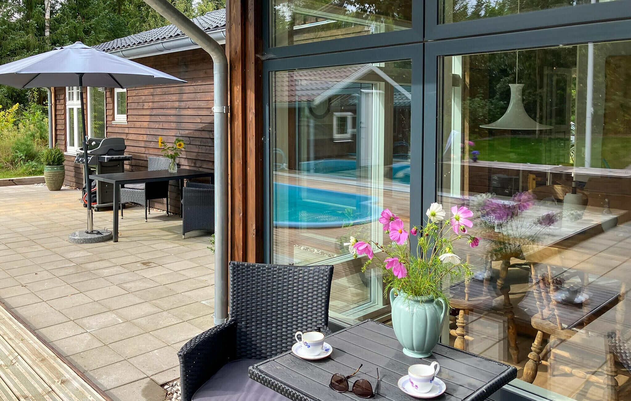 An outdoor patio area with a glass-enclosed pool, wicker furniture, and a table with a vase of flowers.