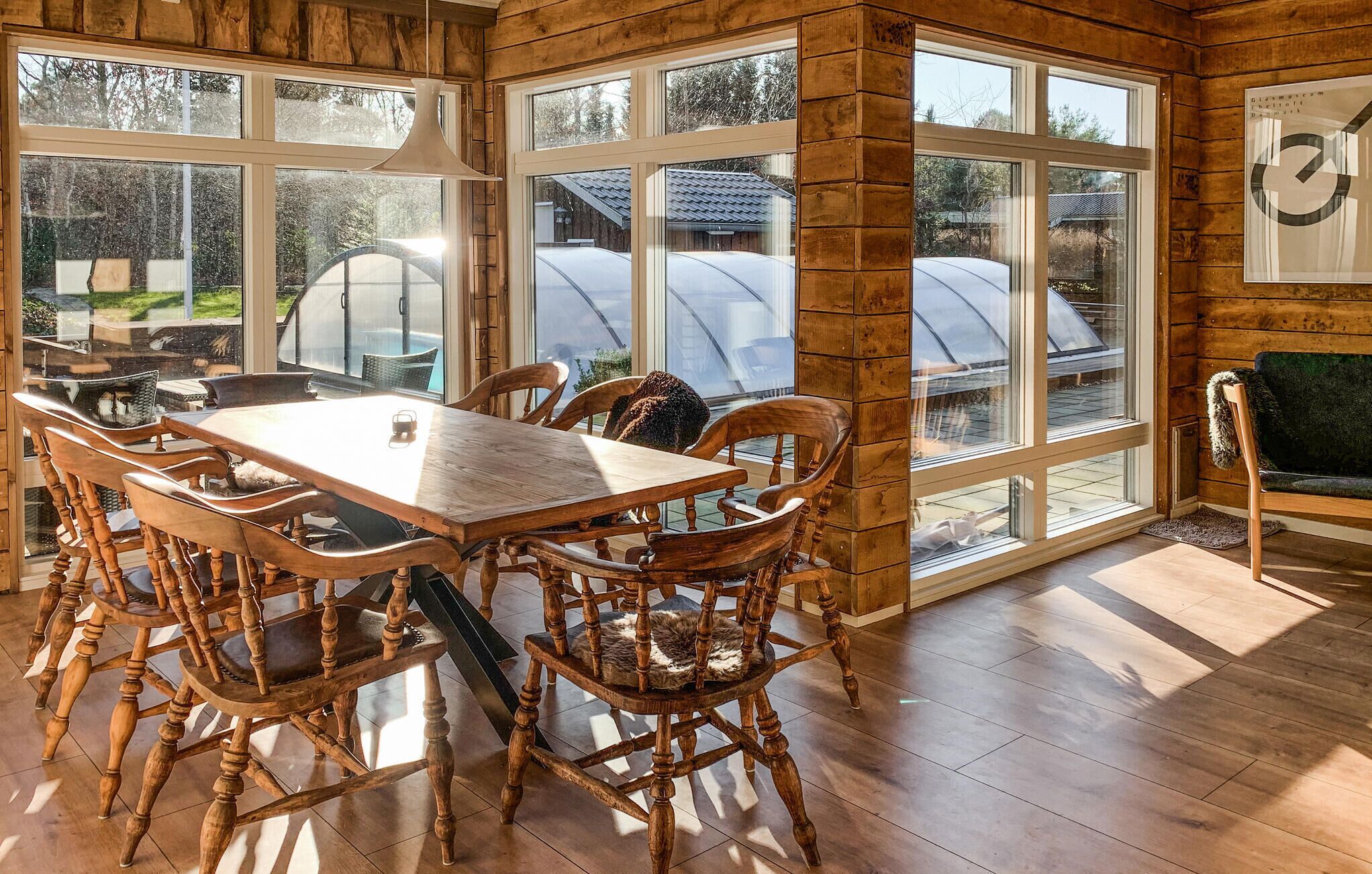 Un espace repas avec une table et des chaises en bois, de grandes fenêtres et une vue sur des serres.