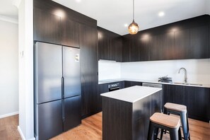 Una cocina moderna con armarios oscuros, un refrigerador de acero inoxidable, una isla central con taburetes e iluminación colgante.