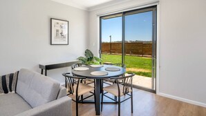 Un salon moderne avec une table ronde, un canapé et une grande porte-fenêtre coulissante donnant sur un espace extérieur verdoyant.