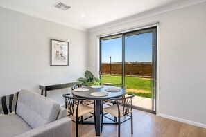 Una sala de estar moderna con una mesa redonda, un sofá y un amplio ventanal corredero que da a un espacio exterior con césped.