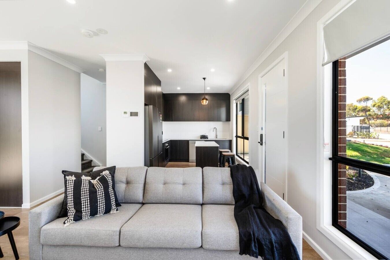 A modern living room with a grey sofa, a black throw blanket, and a checkered pillow.