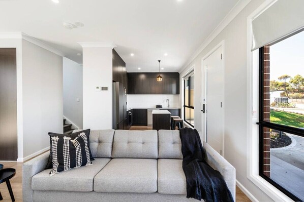 A modern living room with a grey sofa, a black throw blanket, and a checkered pillow.