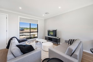 A modern living room with a large window, a flat-screen TV, grey sofas, and a small round table.