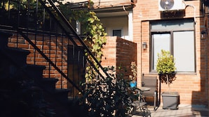 Un edificio de ladrillo con una escalera, plantas en macetas y un pequeño espacio al aire libre con mesas y sillas.