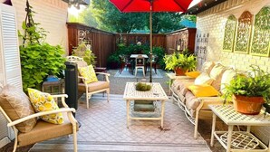Un patio con mobiliario exterior, una sombrilla roja y plantas en macetas.