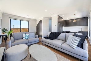 Ein modernes Wohnzimmer mit zwei grauen Sofas, einem runden Couchtisch und einem Essbereich mit Tisch und Stühlen.