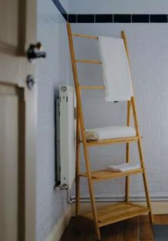 A corner of a room with a wooden ladder shelf against a white wall, a radiator, and a door.