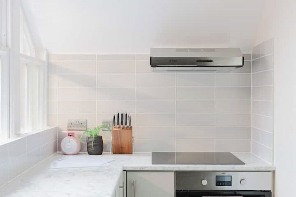 A modern kitchen with white tiles, a built-in oven, and a range hood.