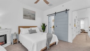 Une chambre à coucher avec un lit, un ventilateur de plafond, une cheminée et une porte coulissante donnant sur une autre pièce.