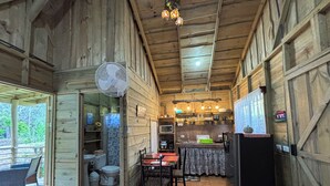 A wooden cabin interior with a dining area, kitchen, and a fan.