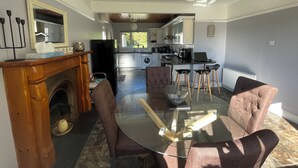 Uma cozinha moderna com armários brancos, uma geladeira preta e um espaço de refeições com mesa de vidro e cadeiras marrons.