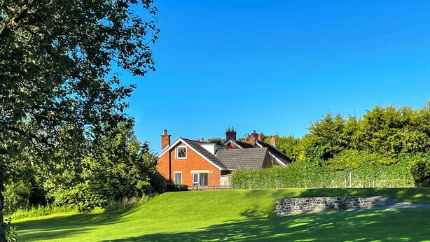 Uma casa com telhado inclinado, fachada de tijolos e uma parede de pedra à frente.