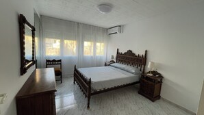 A bedroom with a wooden bed, a bedside table, a chair, a mirror, and a window with curtains.