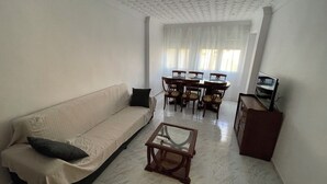 A living room with a sofa, a coffee table, a dining table with chairs, and a television.
