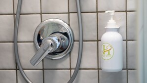 A bathroom with a shower head and a bottle of hand soap on a tiled wall. - Vitti's home Verona 5 (Verona)