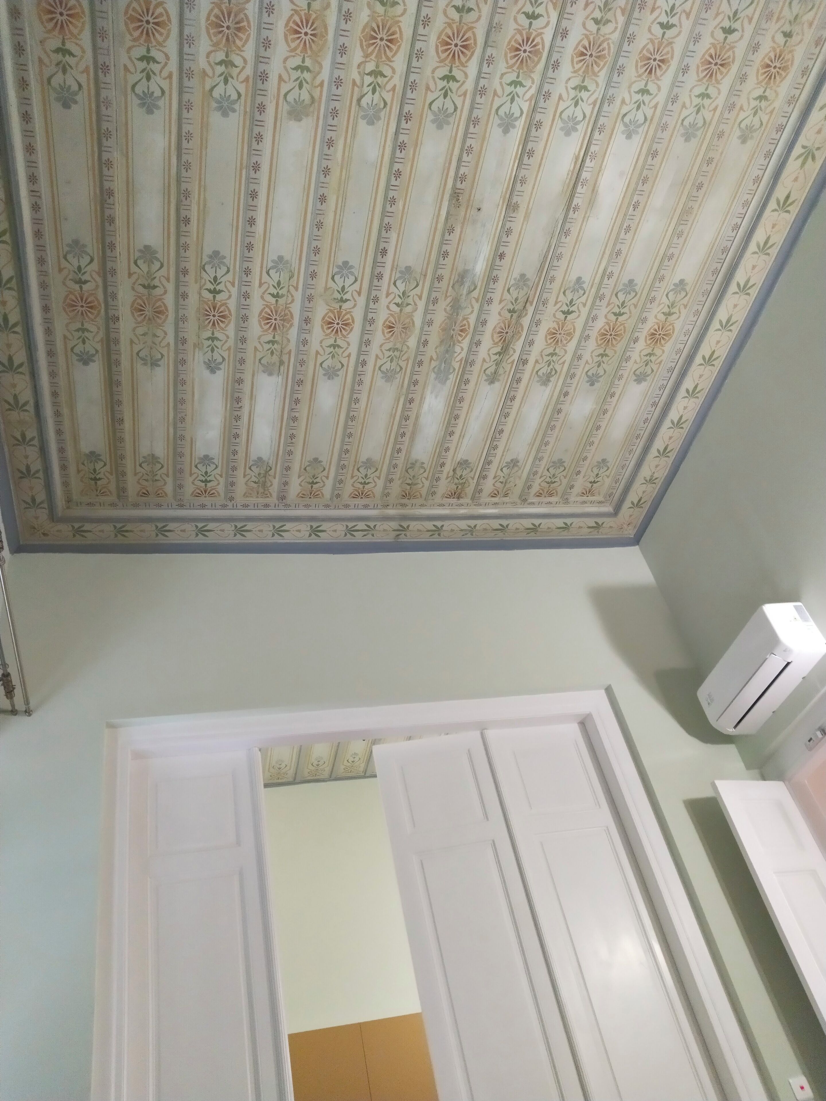 A room with a patterned ceiling, white doors, and an air conditioning unit.