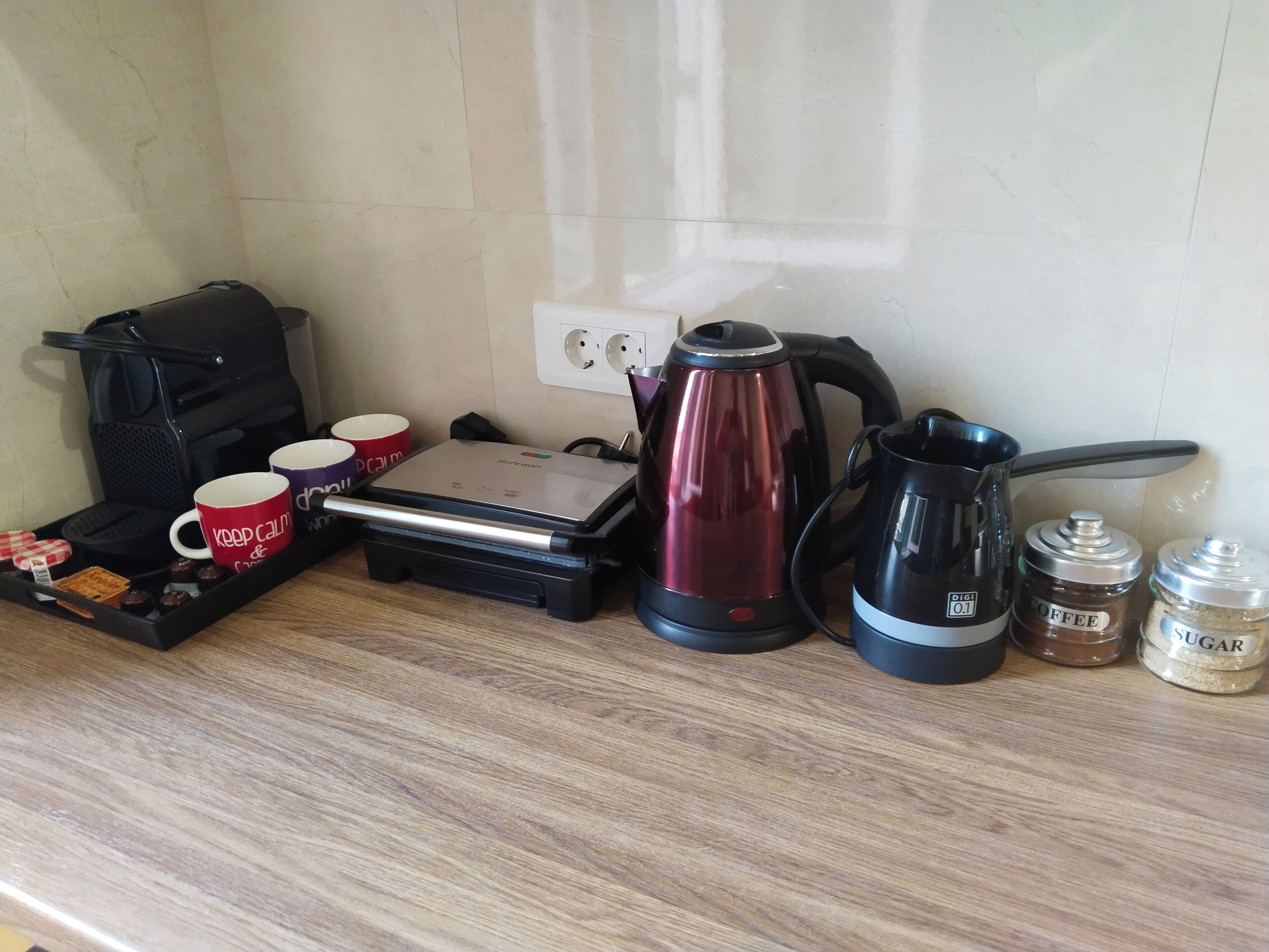 Una encimera de cocina con una cafetera, un hervidor, un molinillo de café y una bandeja con tazas y aperitivos.