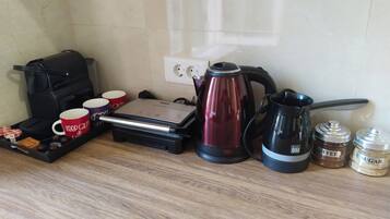 A kitchen counter with a coffee maker, a kettle, a coffee grinder, and a tray with mugs and snacks.