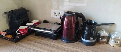 Una encimera de cocina con una cafetera, un hervidor, un molinillo de café y una bandeja con tazas y aperitivos.