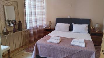 A neatly made bed with white linens and a pink blanket, a bedside table with a lamp, and a mirror on the wall.