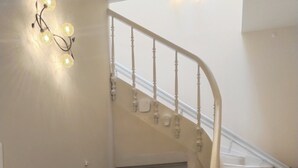 A staircase with a white railing, a dark wooden console table with a framed picture, and a white door at the bottom. - 1920  classic (Kalamata)
