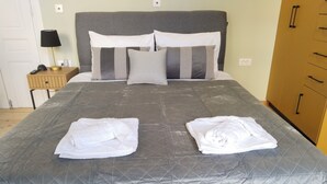 A neatly made bed with a grey quilt and two folded white towels on the bed. - 1920  classic (Kalamata)