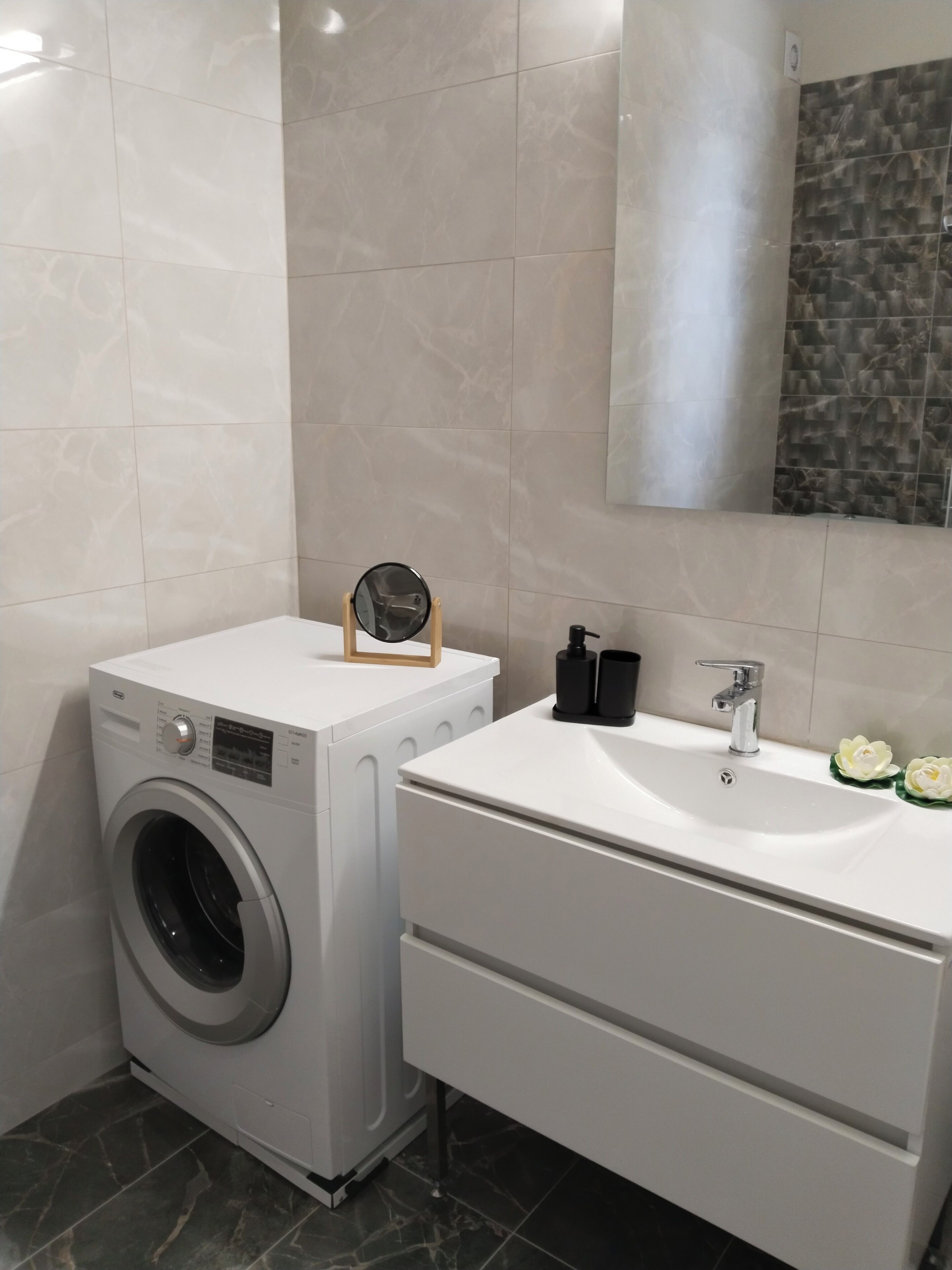 Ein kleines Badezimmer mit einer Frontlader-Waschmaschine, einem weißen Waschtisch mit Spüle und einem Spiegel darüber.